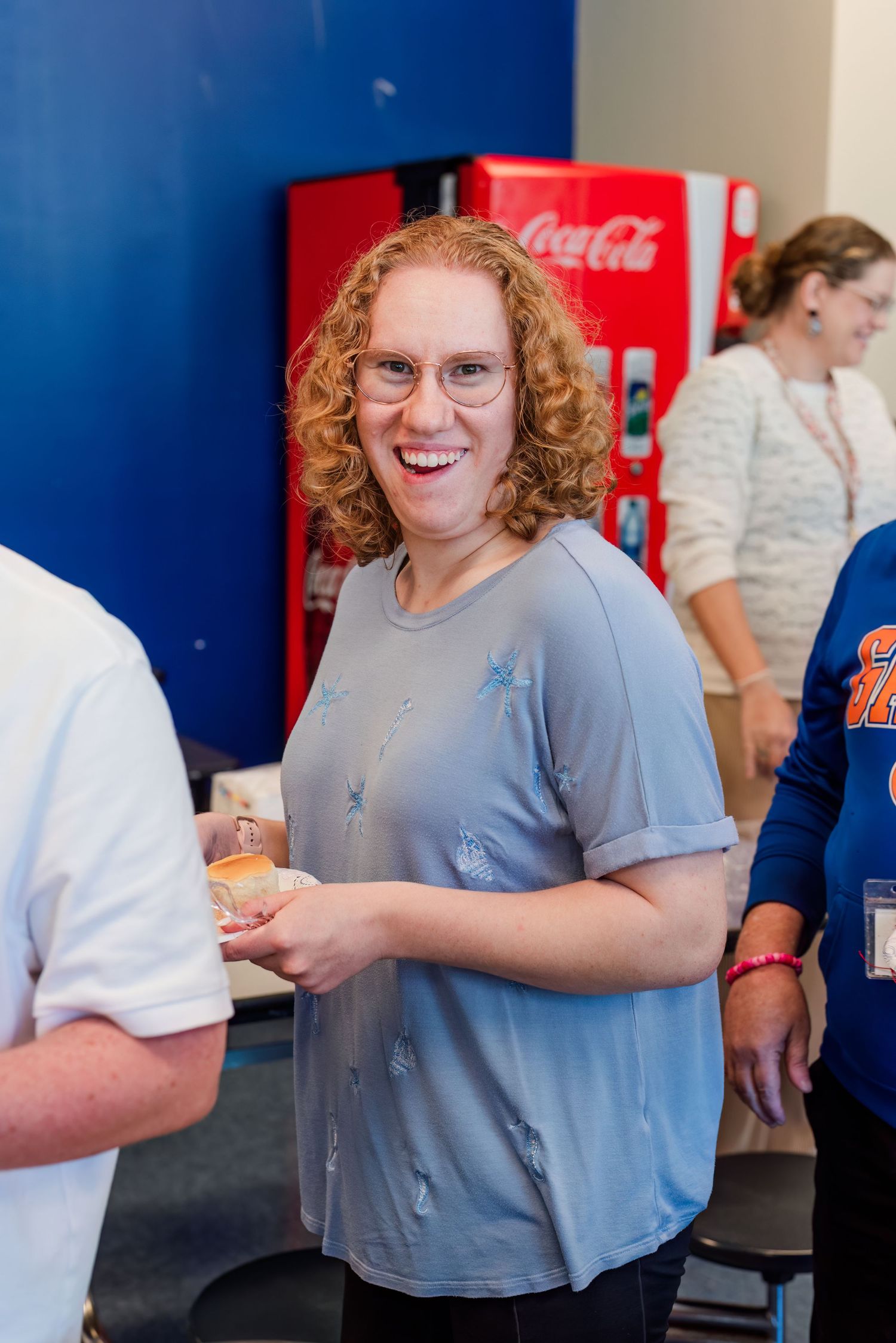 Students gather around red Coca-Cola vending machines in a school hallway with blue walls.