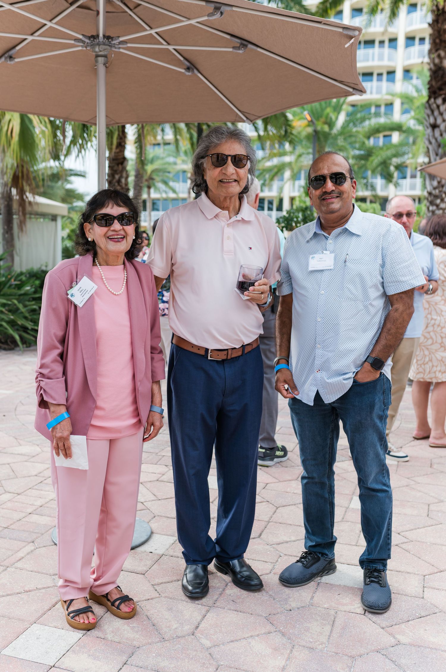 Three smiling people pose outdoors under a patio umbrella at a tropical resort event.