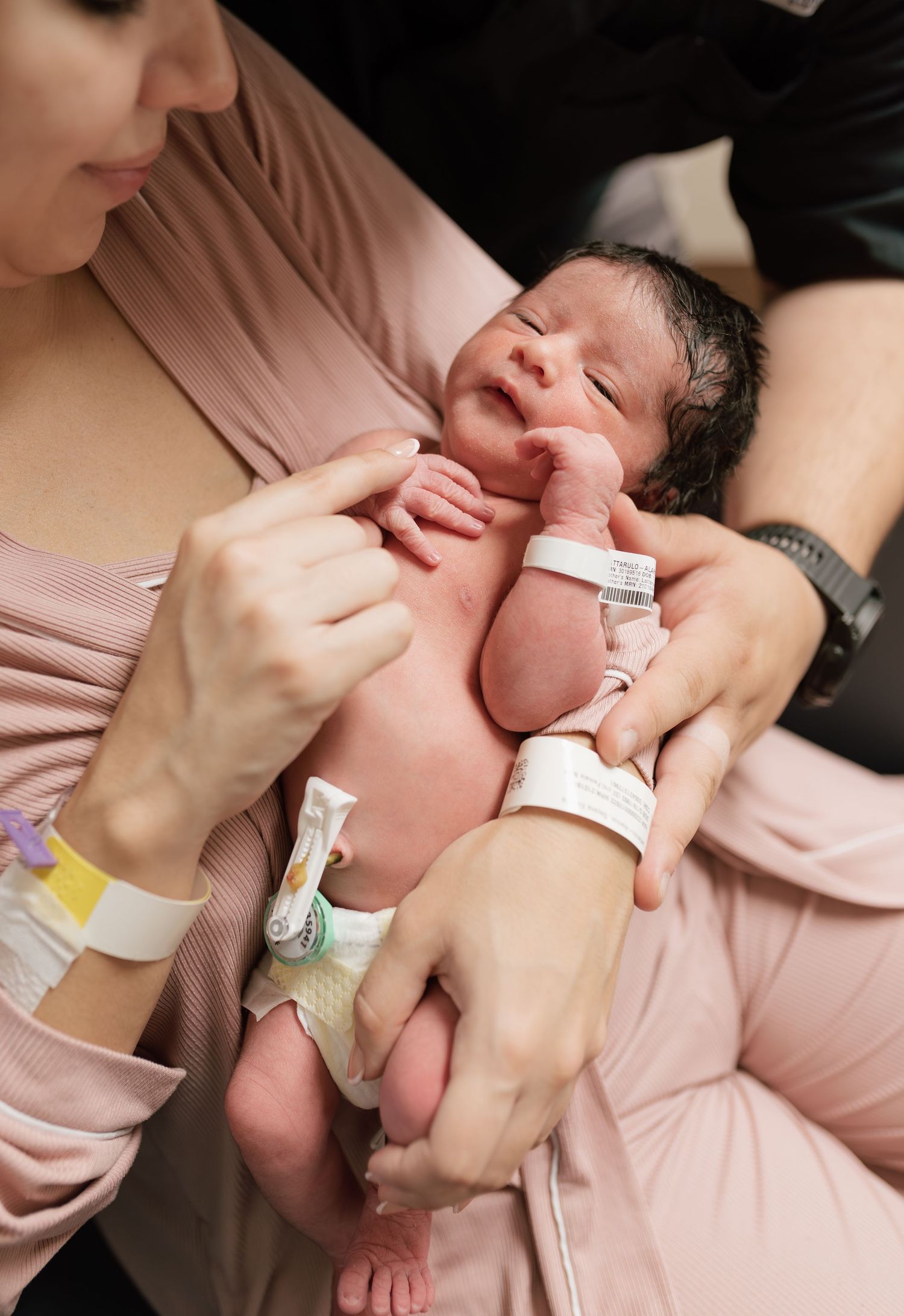 Newborn baby held by mother in hospital room shortly after birth, wearing ID bracelet.