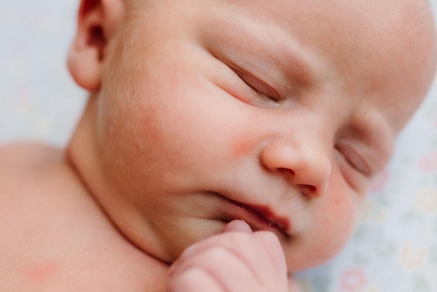 A sleeping baby with closed eyes and a peaceful expression rests with one hand near their mouth.