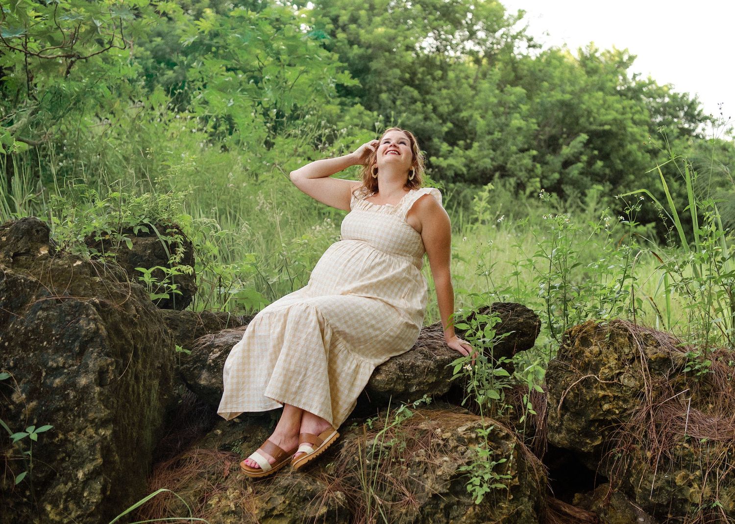 A woman in a flowing white dress reclines on a mossy rock formation in a lush green forest setting.