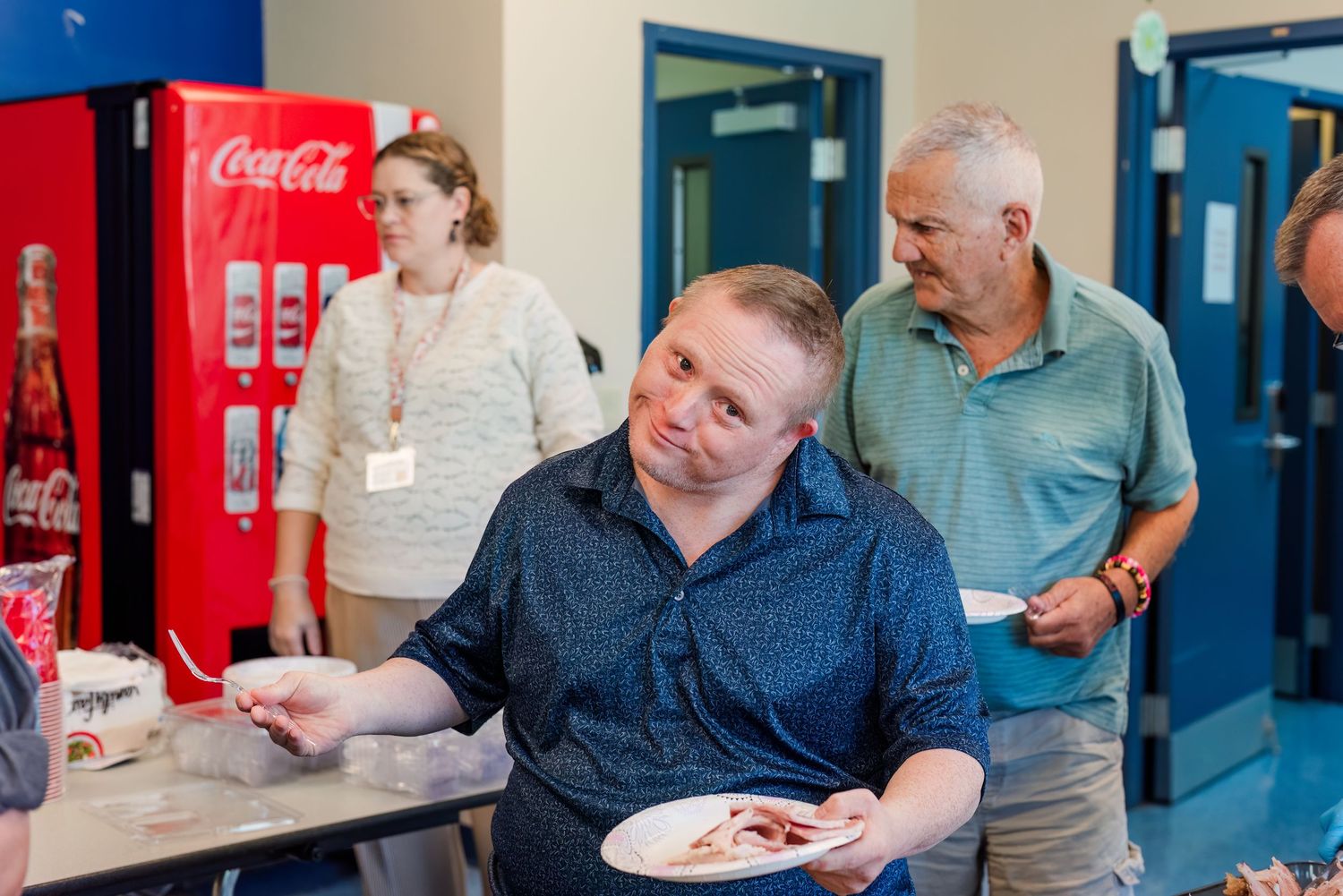 People gather around tables in a casual dining area with blue walls and a Coca-Cola sign visible in the background.