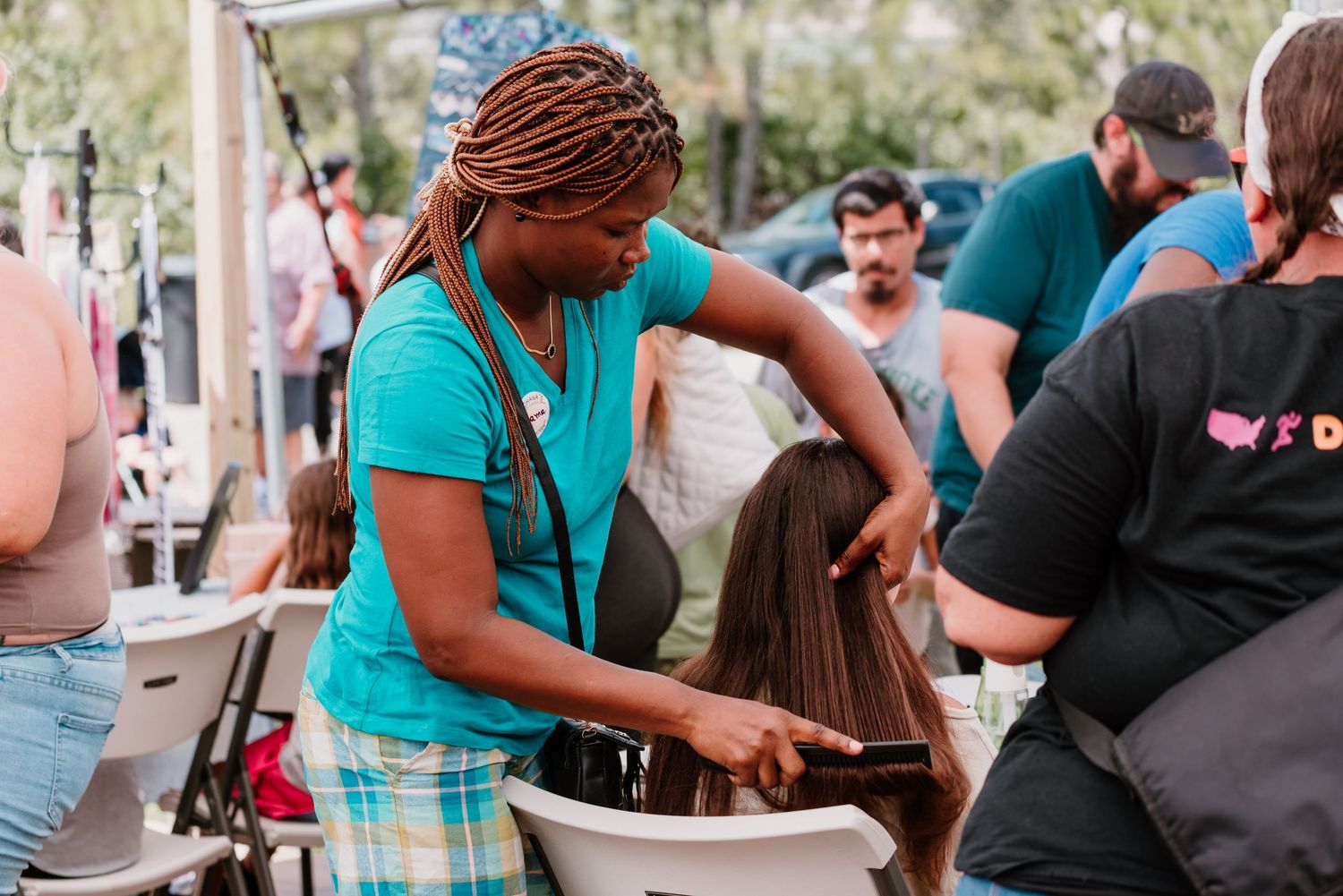 A person in a teal shirt prepares food at an outdoor event while stirring ingredients in metal containers.