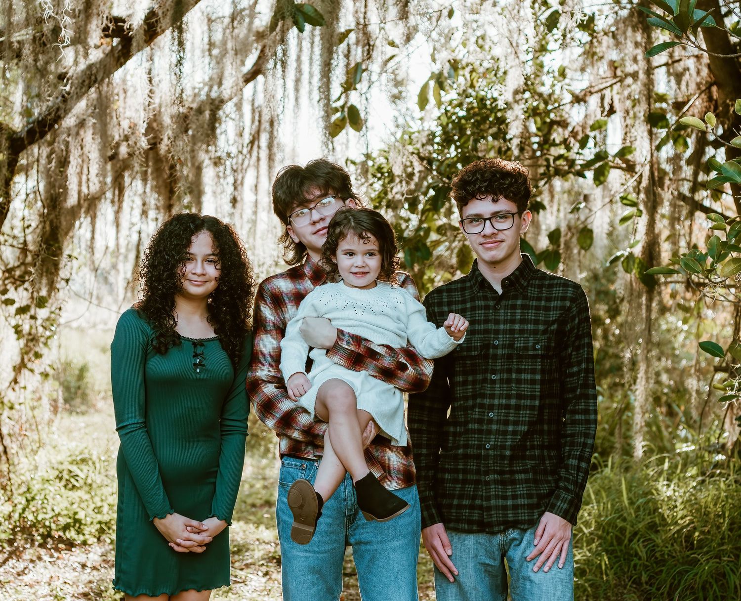 A small group stands together outdoors with mossy oak trees and Spanish moss hanging in the background.