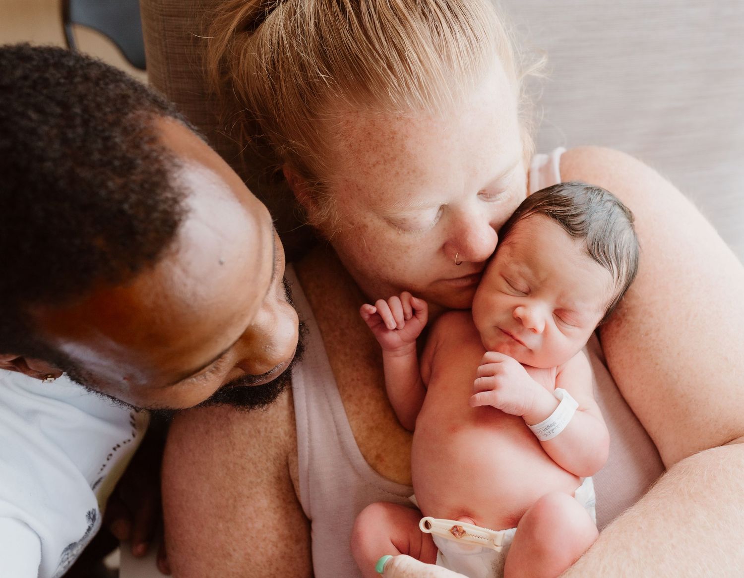 Parent lovingly embracing and nuzzling newborn baby in soft natural lighting.
