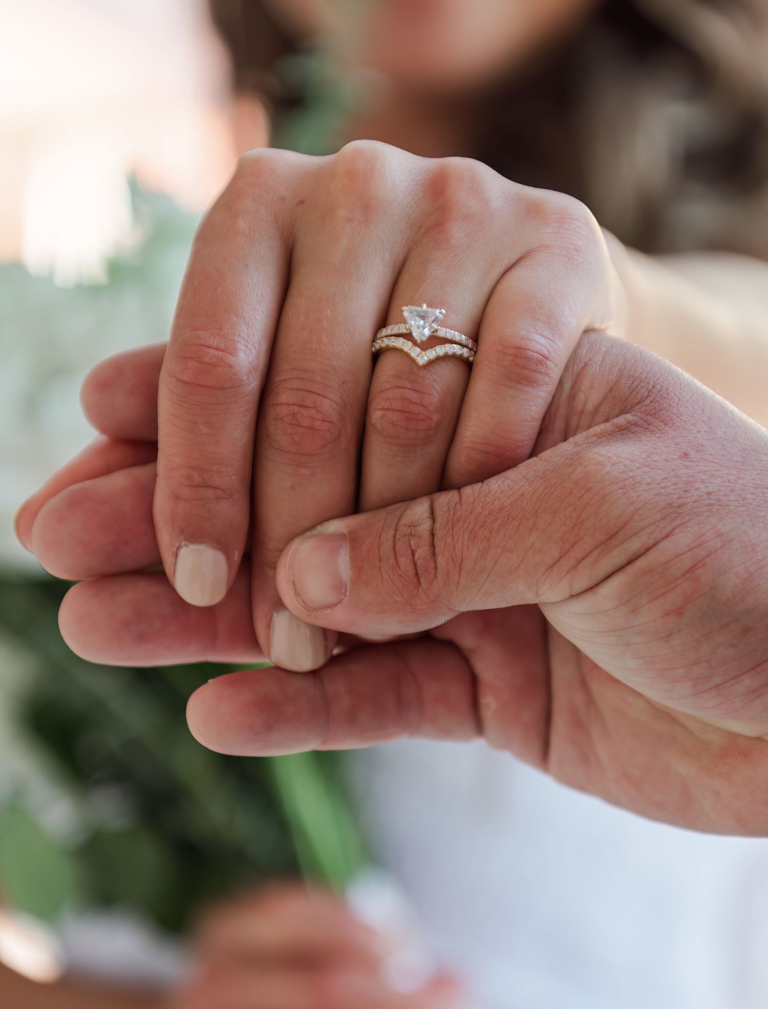 Close-up of bride's hand showing pear-shaped diamond engagement ring with chevron wedding band in gold.