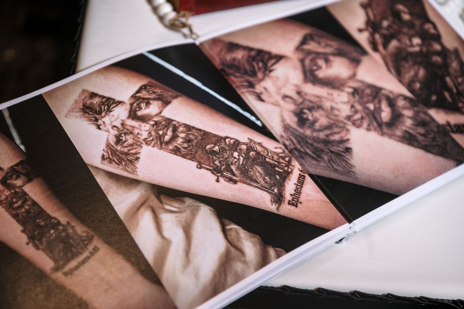 Photos of detailed tattoo designs on forearms displayed in a tattoo portfolio book on a table.