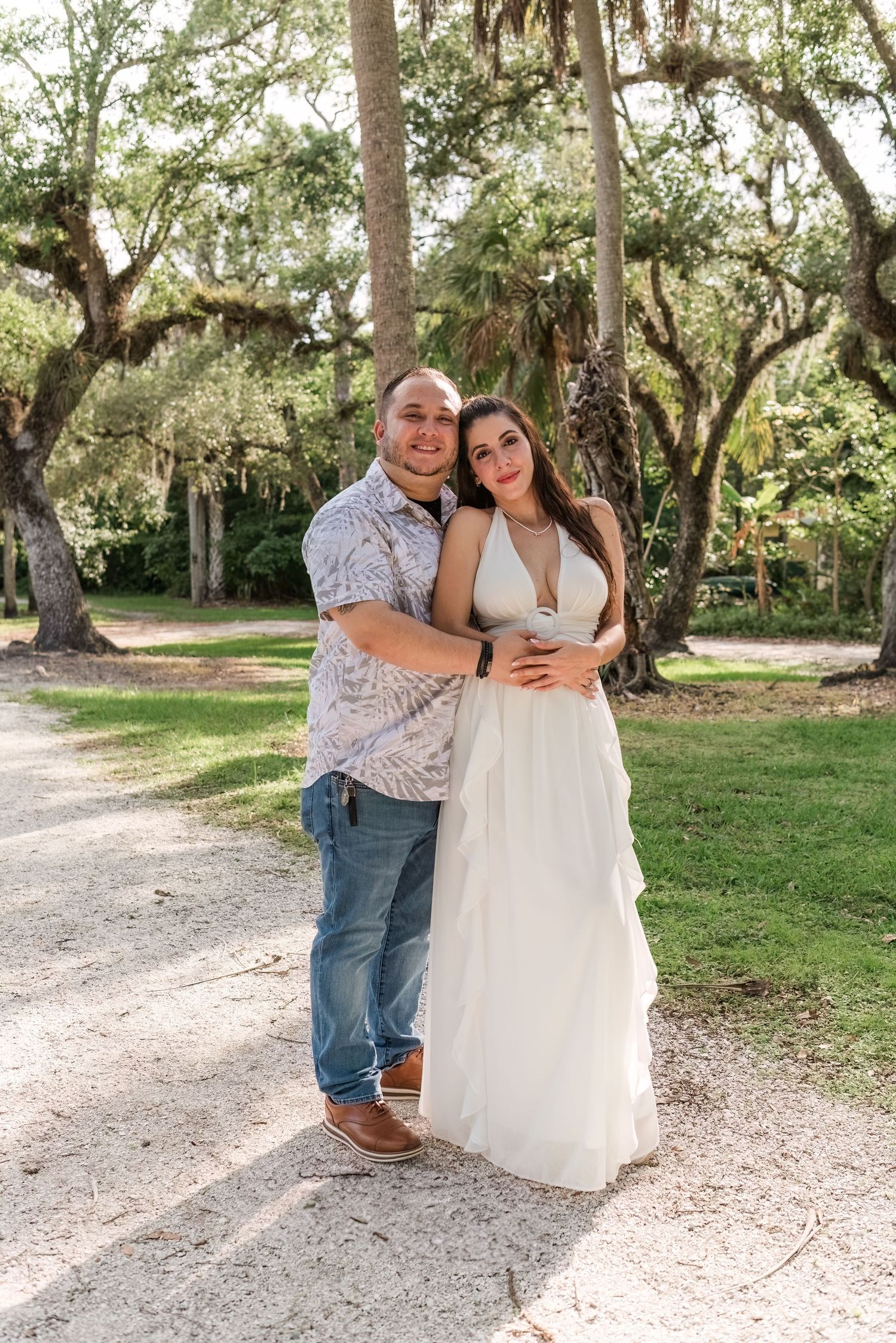 Two people embrace on a scenic path surrounded by oak trees draped in Spanish moss at an outdoor venue.
