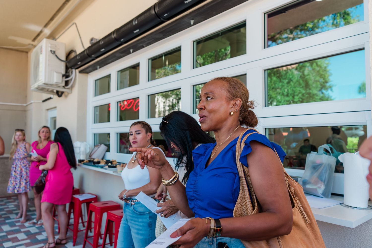People gathered on a covered patio with white columns, engaged in animated conversation and socializing.
