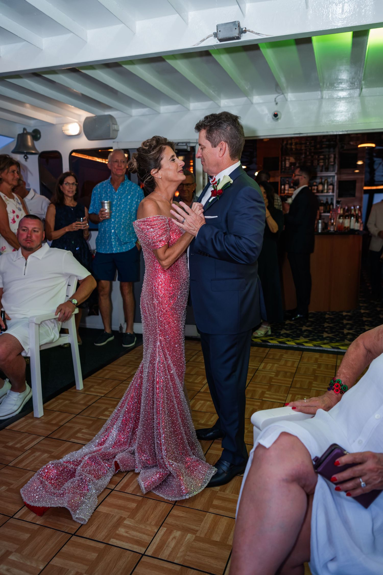 Couple shares first dance in pink sequin gown and navy suit at indoor wedding reception.