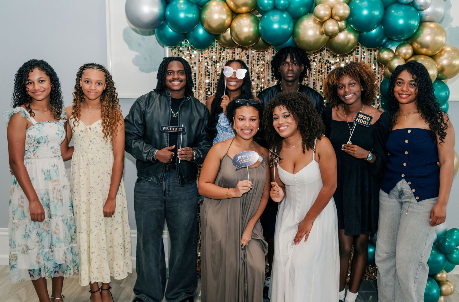 Group of friends posing together at a festive party with teal, gold, and white balloon arch backdrop.