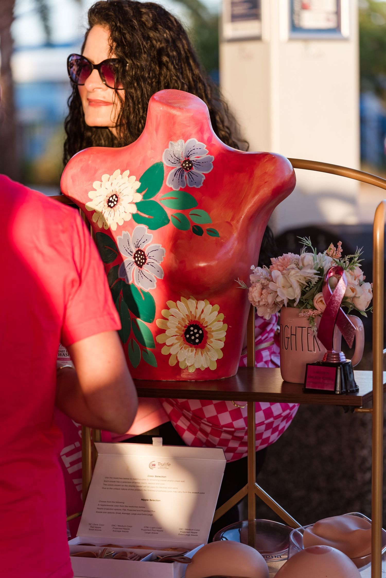 A vibrant red floral dress with green leaves and white blooms is worn while sitting at a table outdoors.