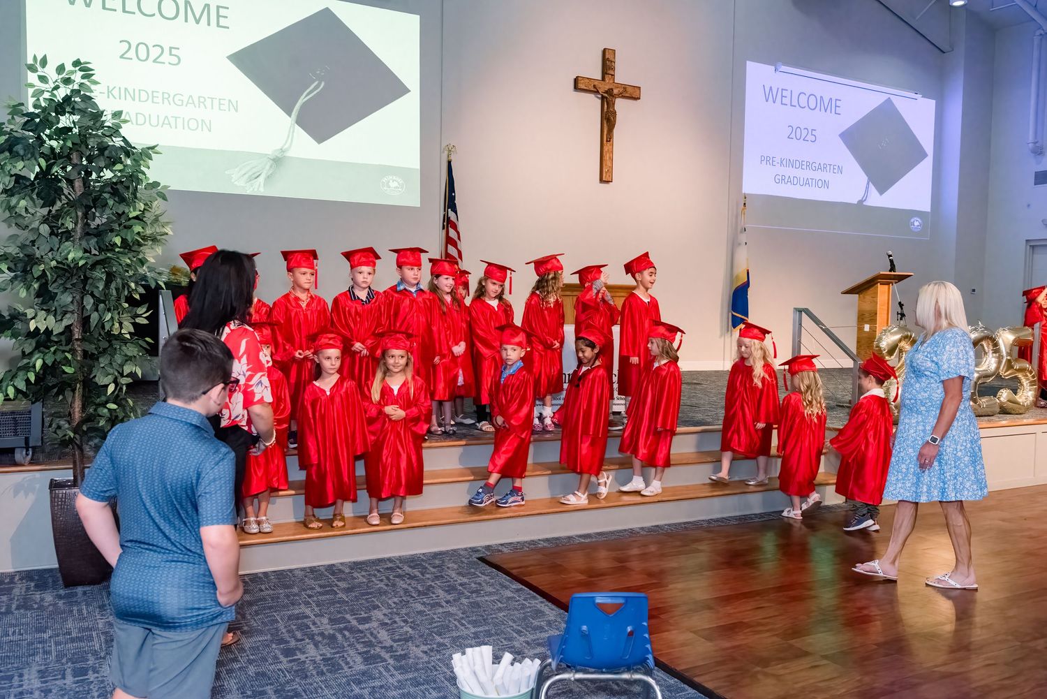 Graduates in bright red caps and gowns line up inside a church during a graduation ceremony.