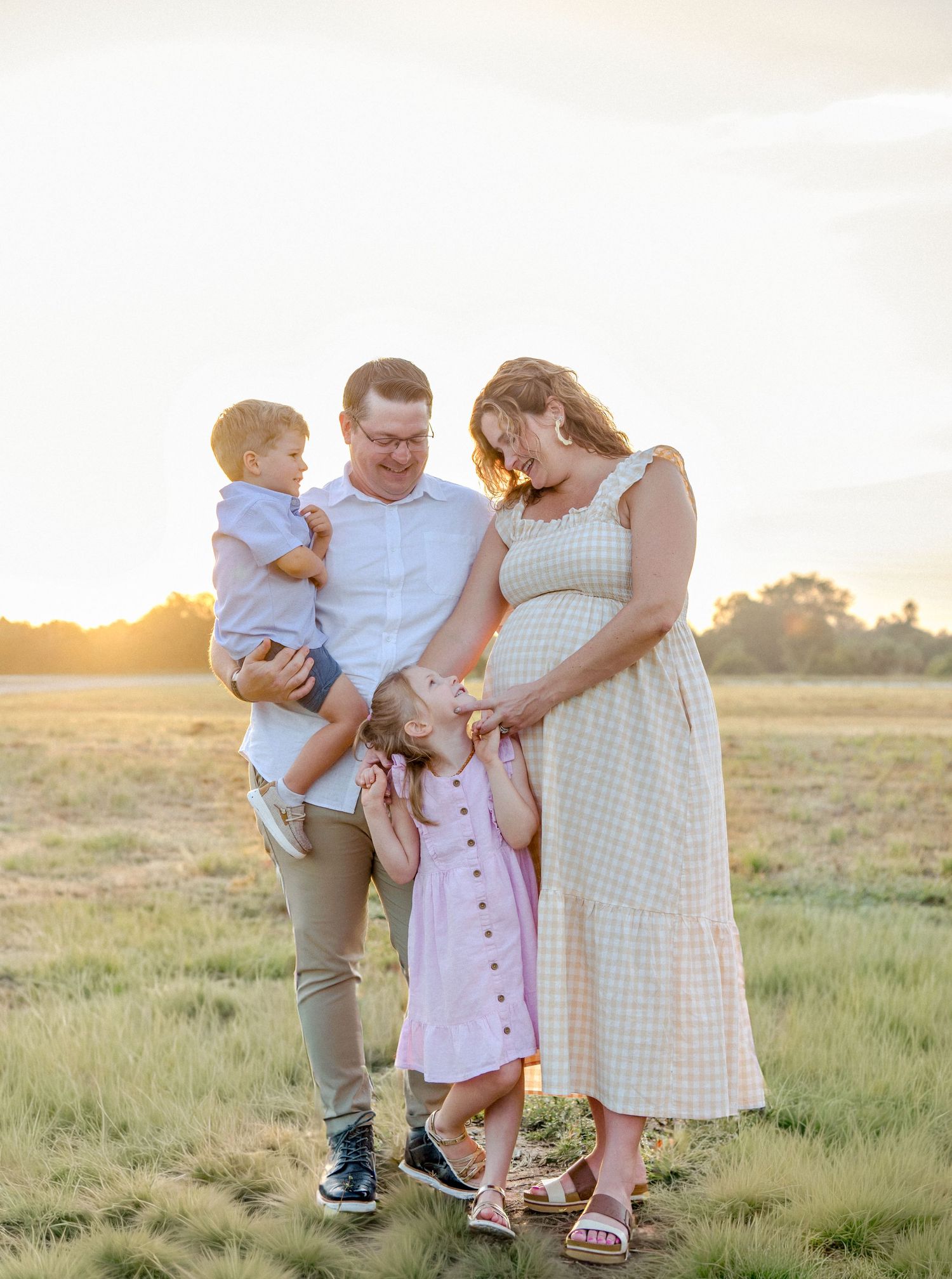 Family enjoying a tender moment together in a sunlit meadow at golden hour.