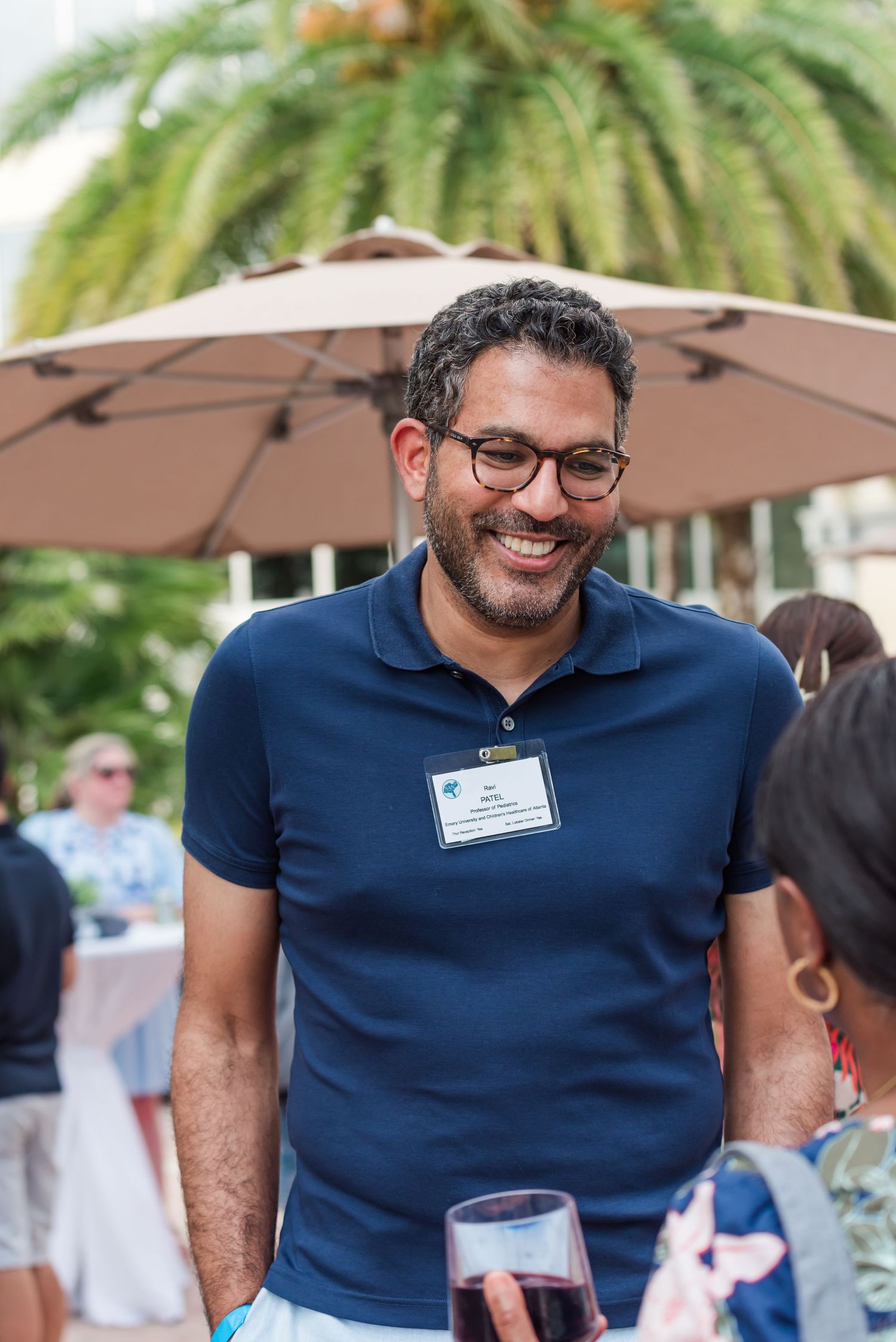 Smiling man wearing glasses and navy polo shirt with name tag at an outdoor networking event.