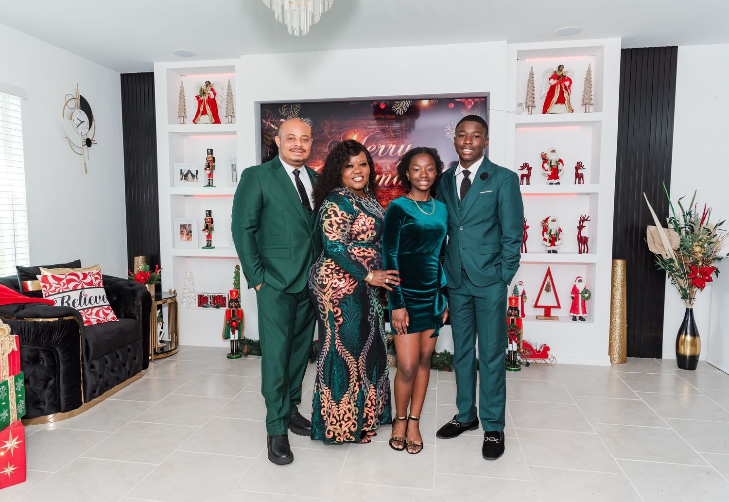 Four people pose in front of a white and red backdrop at a formal event wearing green suits and elegant attire.
