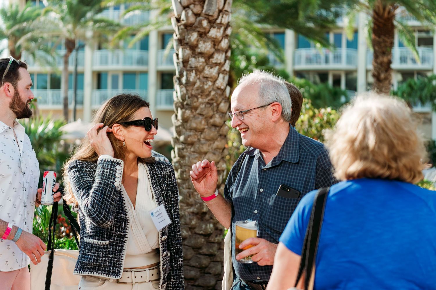 Group of people socializing and chatting near palm trees at an outdoor event.