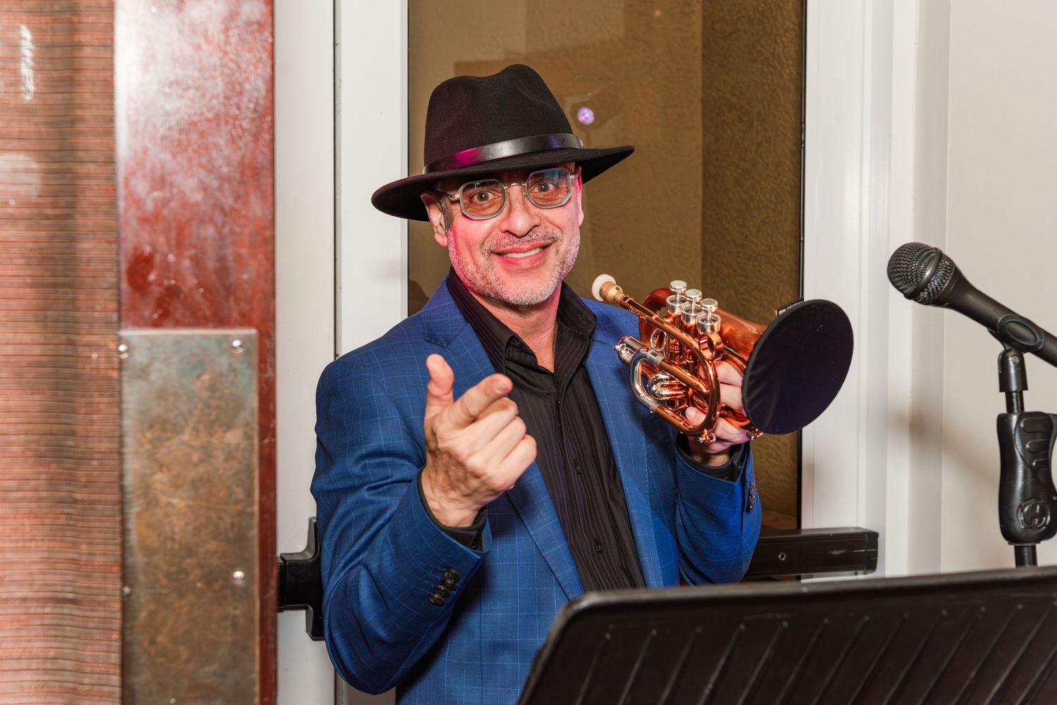 Musicians in blue attire and hats perform on stage at an indoor venue with brick walls.
