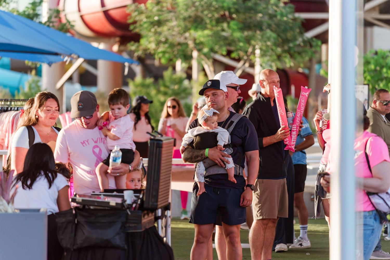 A crowd of people wearing pink shirts gather outdoors at a breast cancer awareness event.