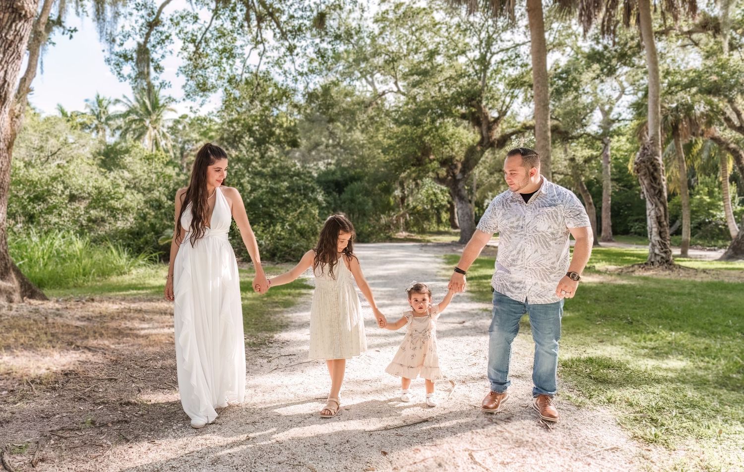 Family walking together and holding hands on a sunlit trail surrounded by palm trees and lush greenery.