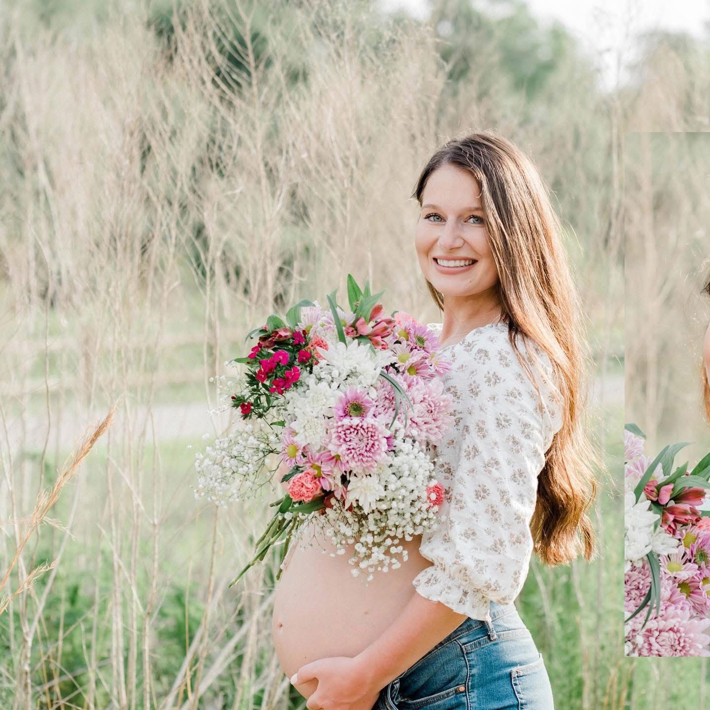A pregnant woman in denim and lace holds a bouquet of pink flowers while smiling in a field of tall grass.