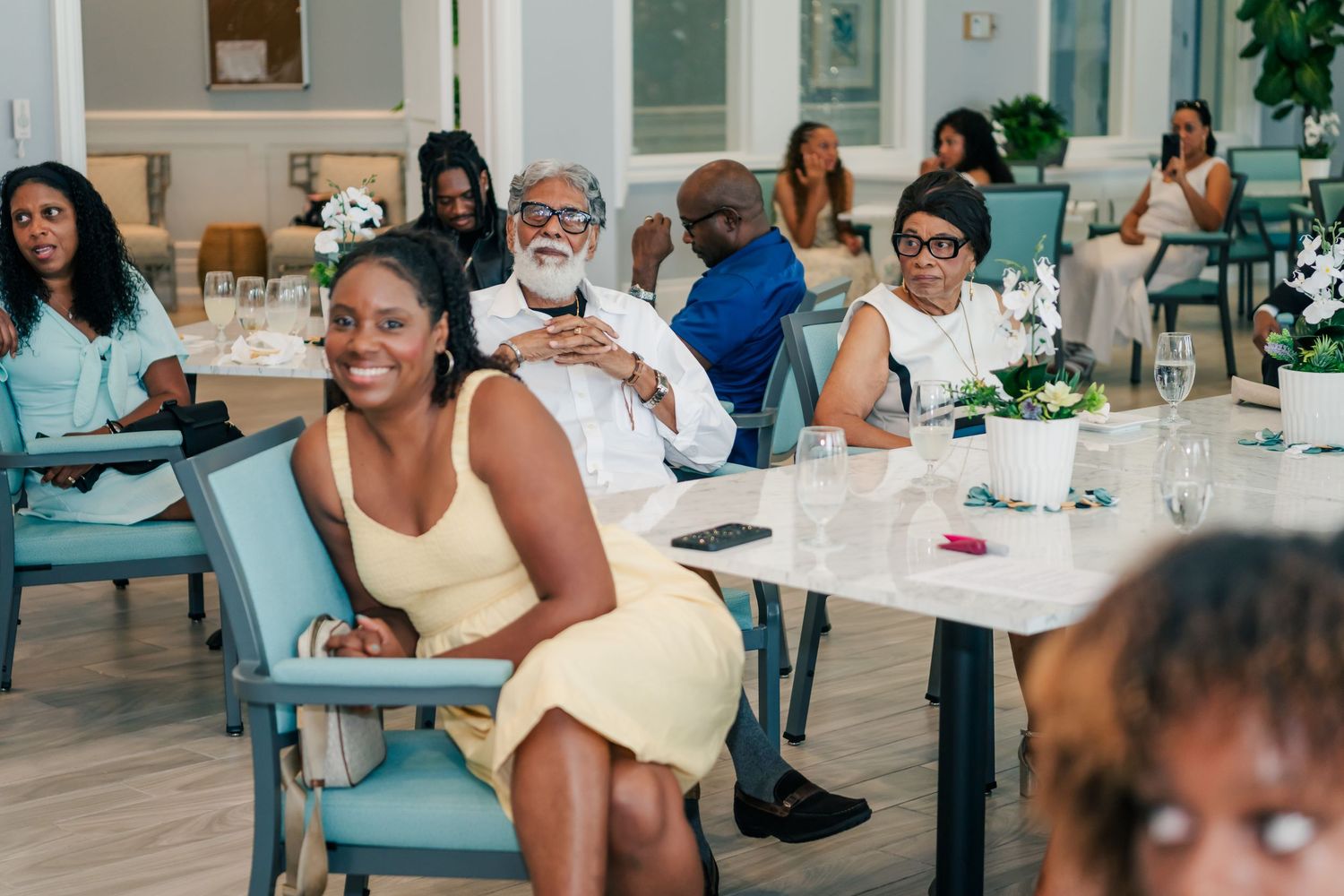 Group of people seated at tables in a bright restaurant, smiling and enjoying an event together.