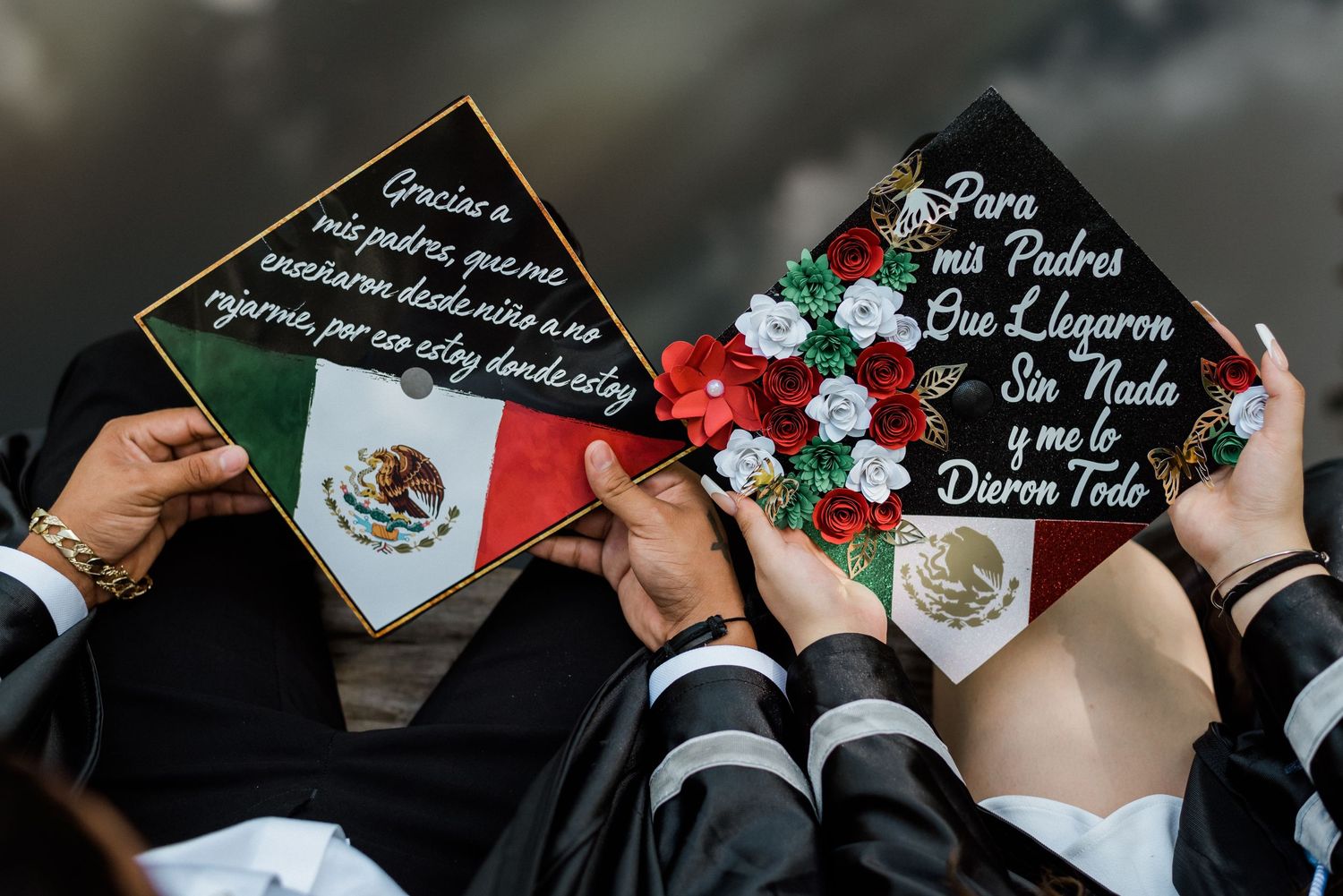 Two graduation caps decorated with Mexican flag and Spanish text are held up during commencement ceremony.
