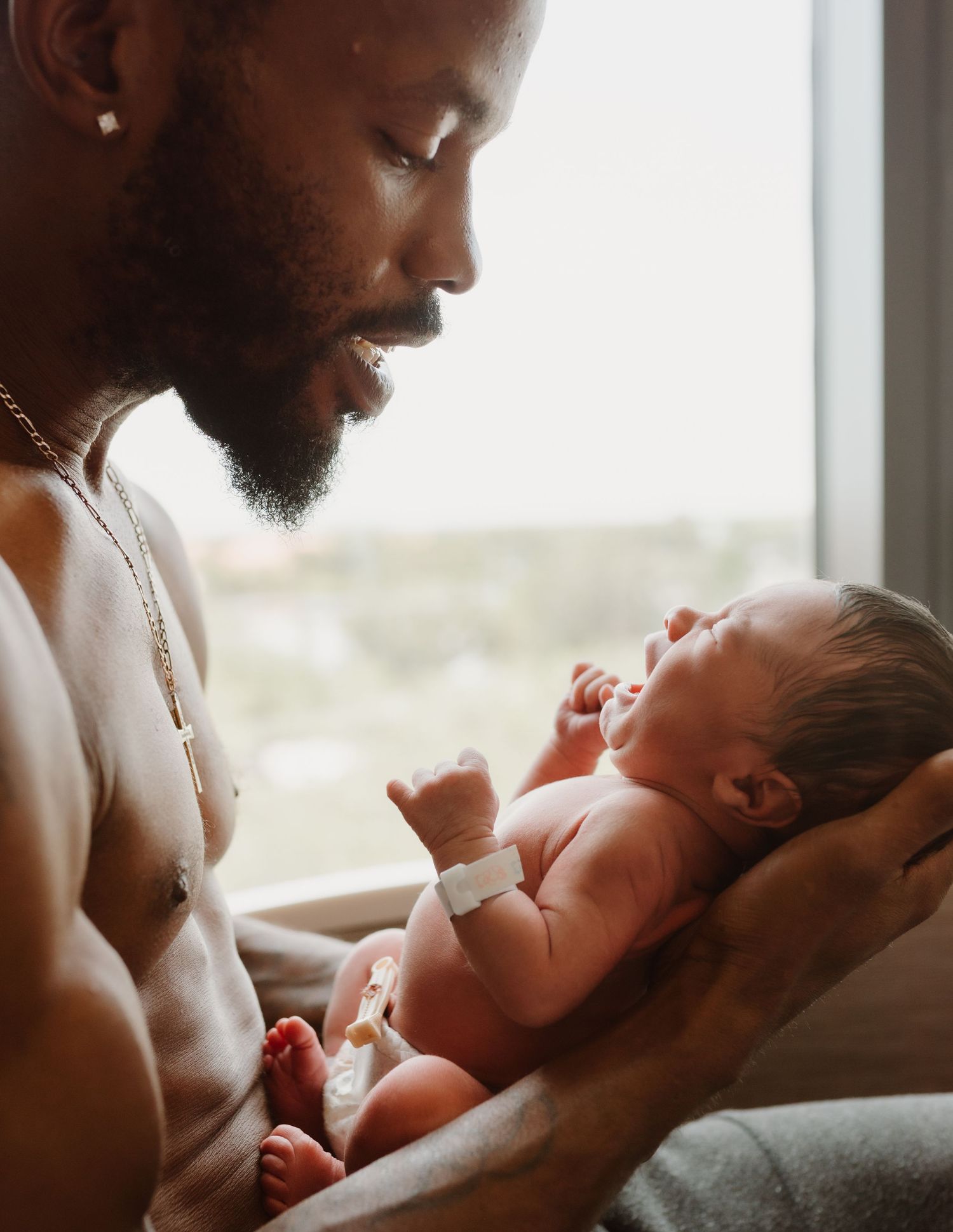 A tender moment captured near a window as a loving parent cradles and gazes down at their newborn baby.