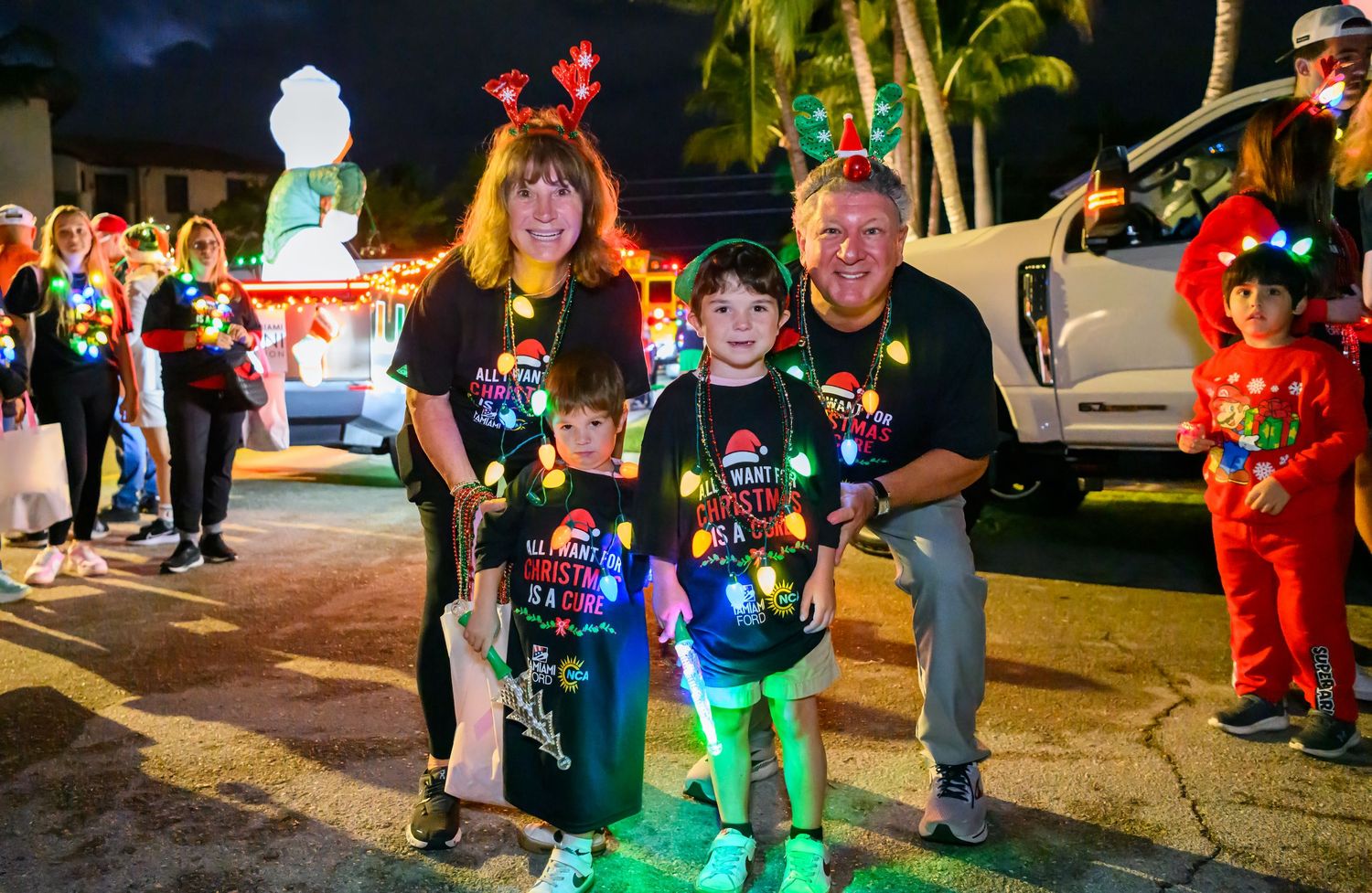 People walking through outdoor holiday light display with palm trees and red decorations.