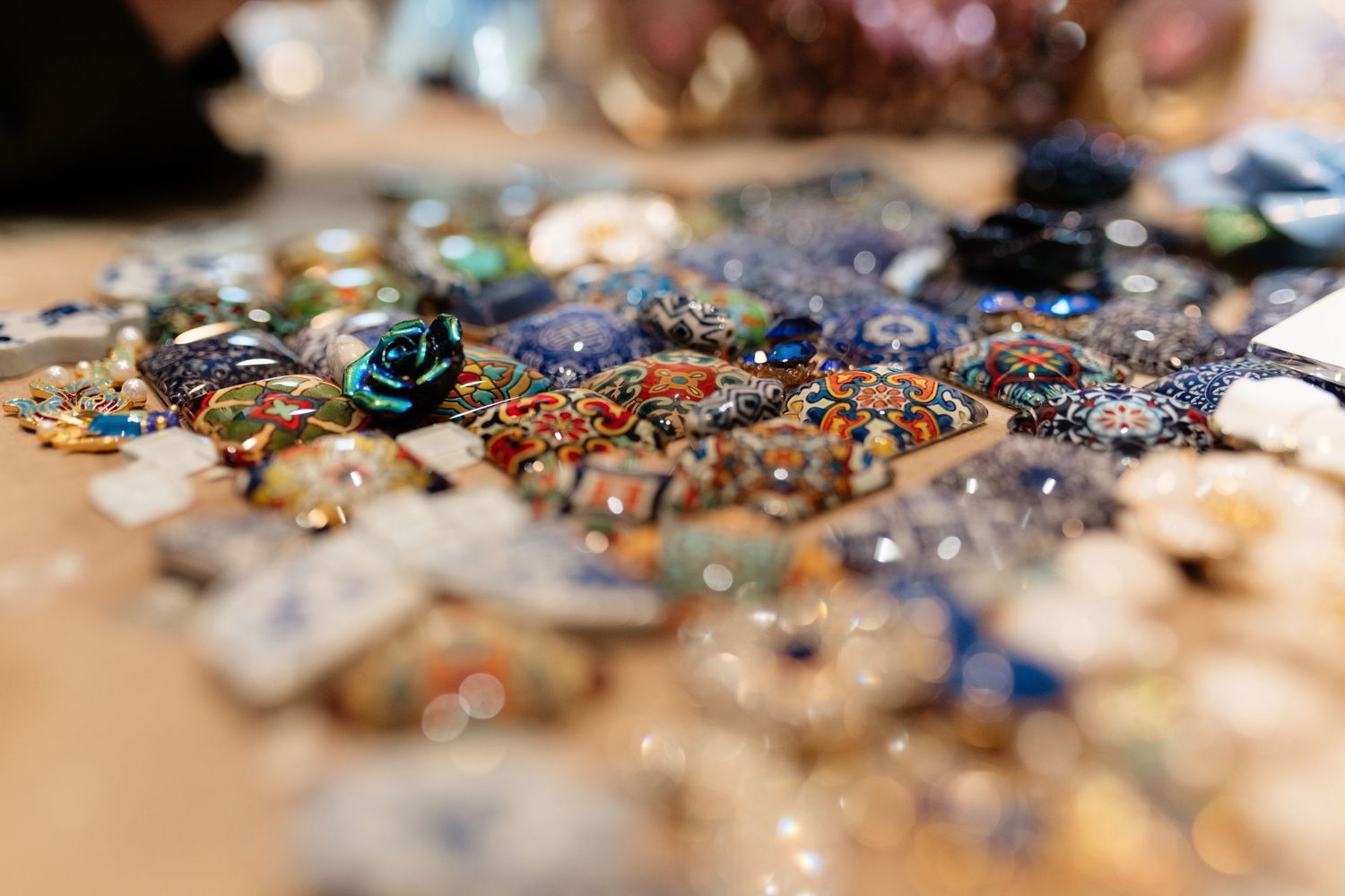 Close-up of colorful mosaic jewelry pieces with beads, gems, and a teal rose on a wooden surface.