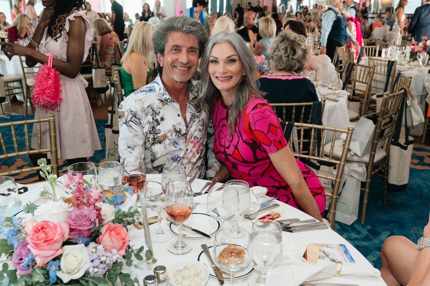 Guests seated at elegant round tables decorated with pink floral centerpieces at a formal banquet event.