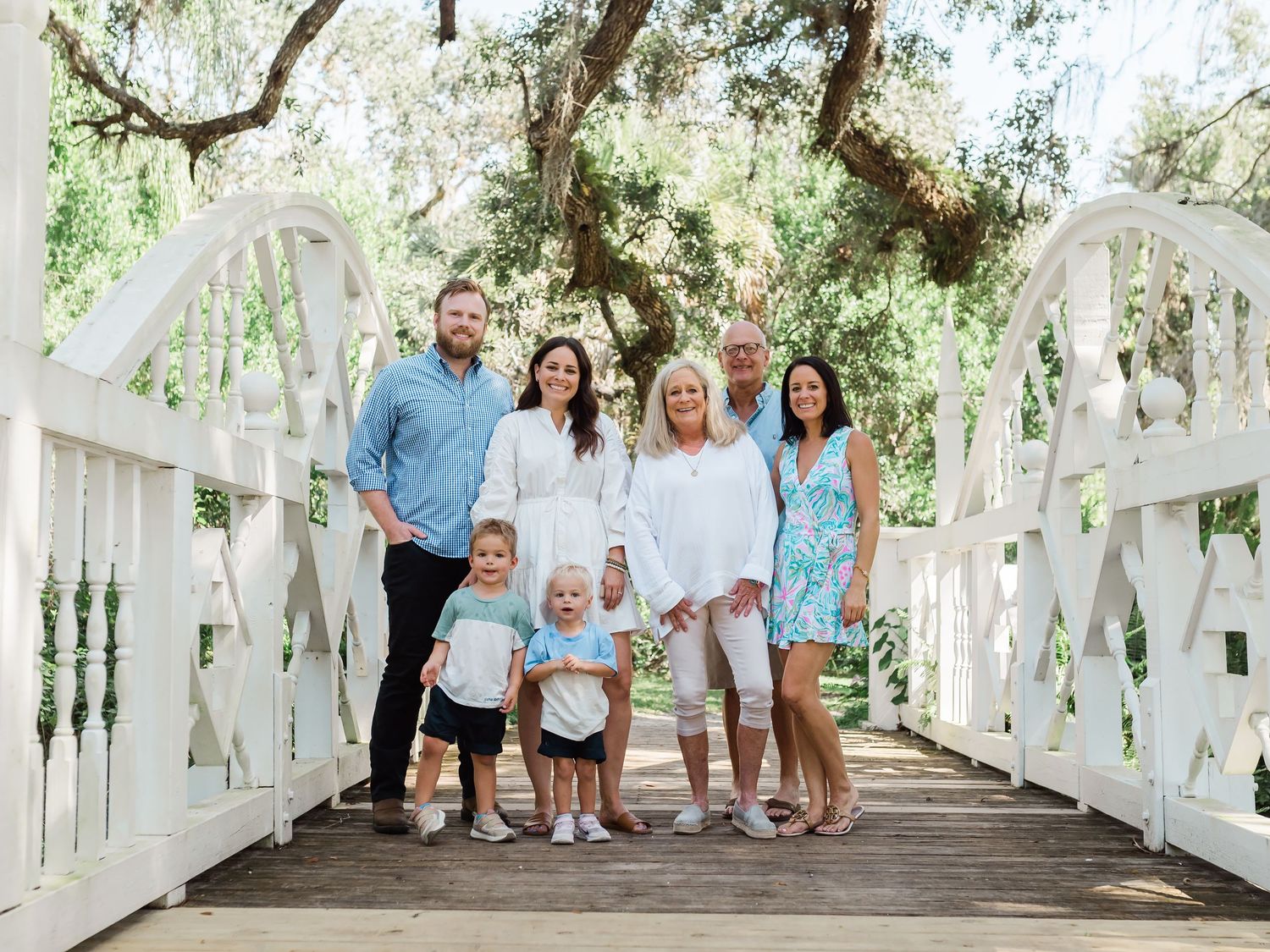 A group portrait taken on a white wooden bridge surrounded by lush greenery on a sunny day.