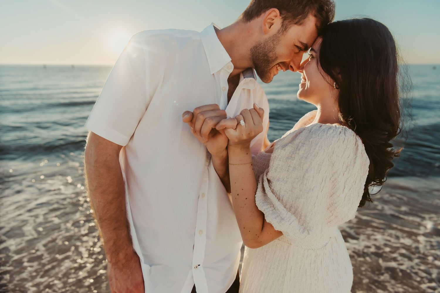A romantic couple shares an intimate moment at sunset on a beach with ocean waves in the background.