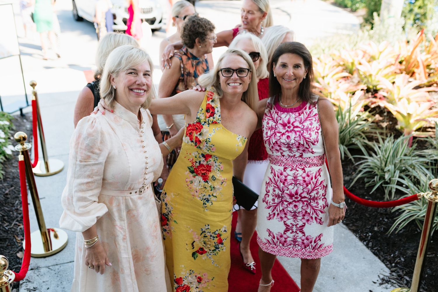 A group in yellow and floral dresses pose together at a summer garden party event.