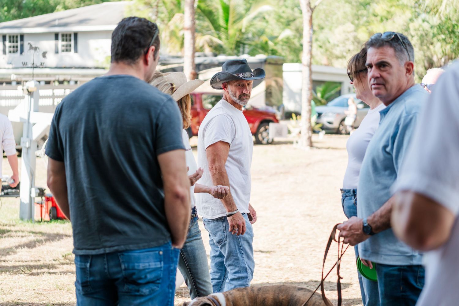 People gather outdoors at a casual event, conversing in small groups on a sunny day.