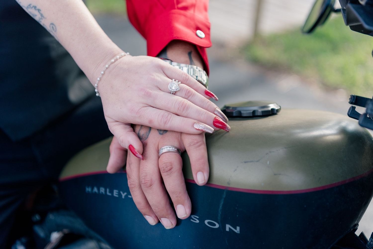 Close-up of hands with red nail polish and engagement ring resting on a Harley Davidson motorcycle.
