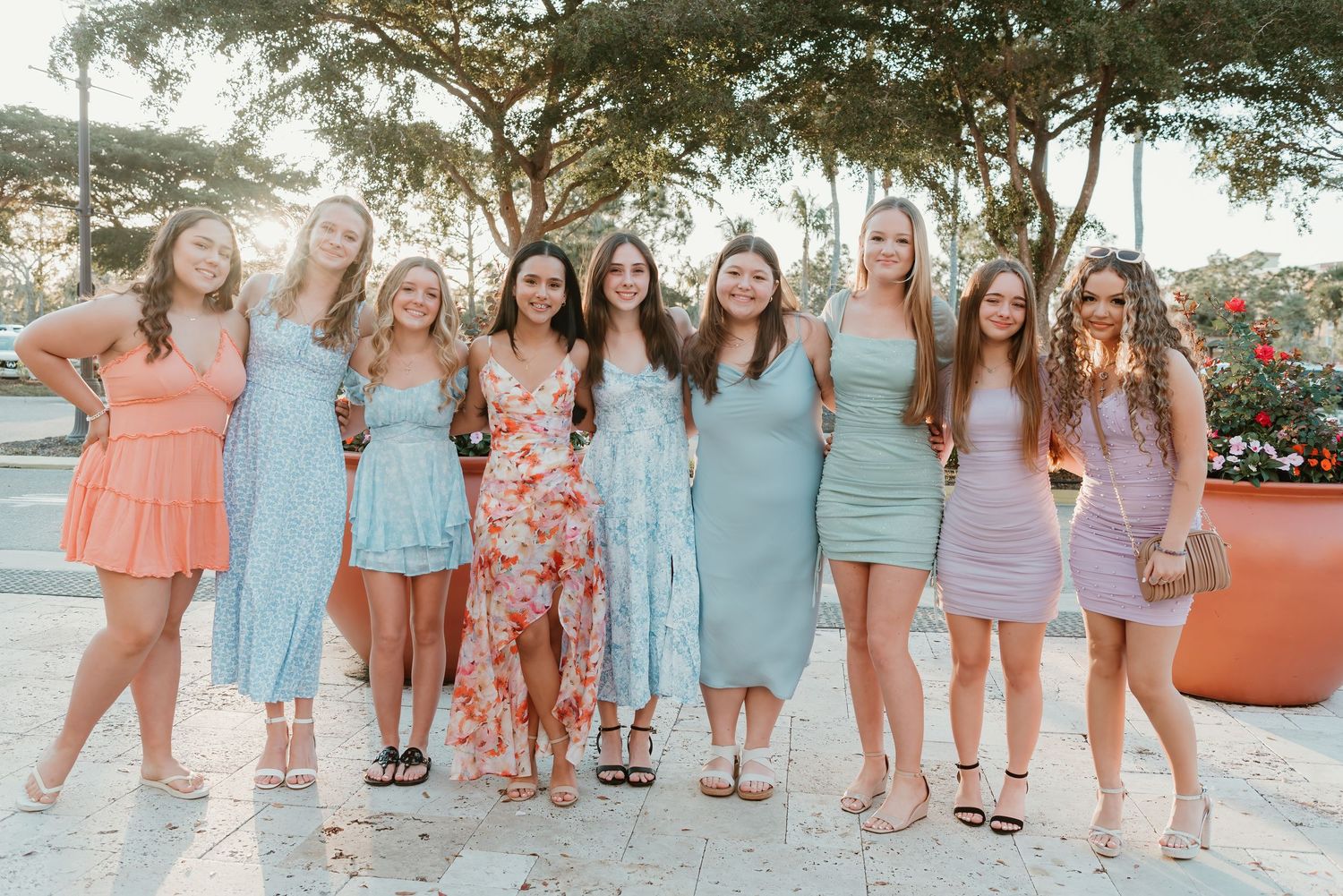 A group of women wearing pastel summer dresses pose together on a sunny outdoor patio.