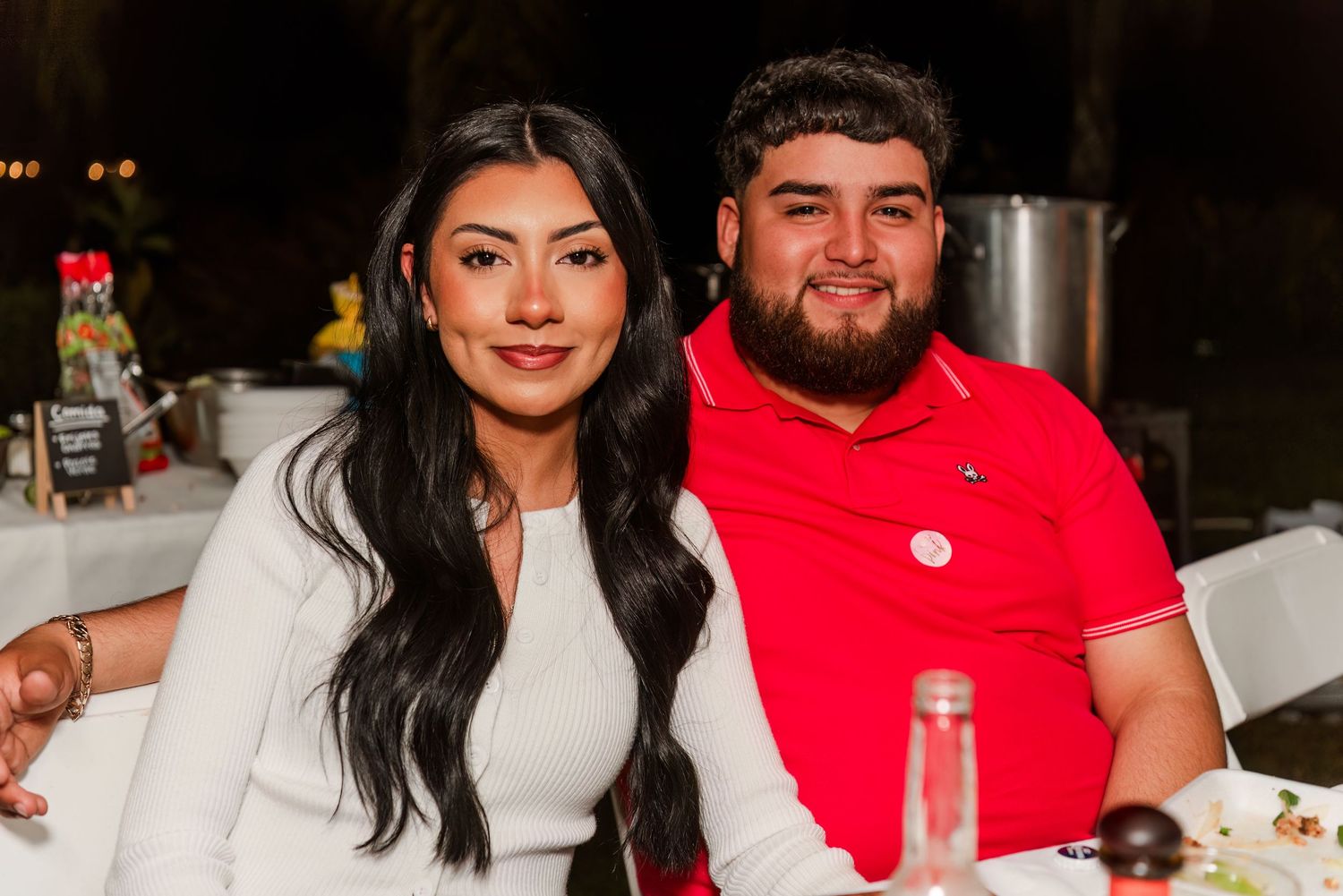 A couple sits together at a restaurant table, with the woman in white and the man in a red polo shirt.