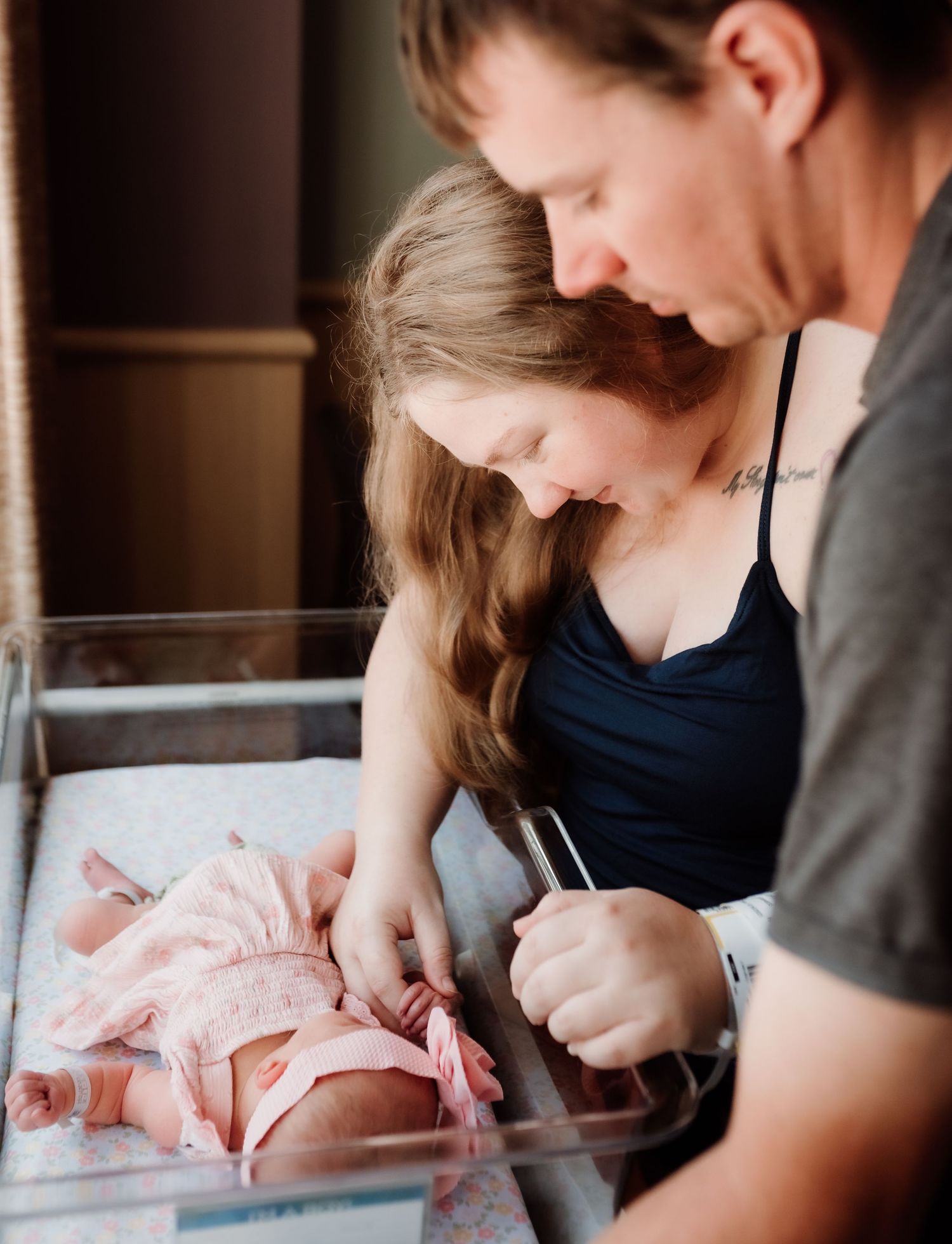 Parent tenderly caring for newborn baby in hospital room setting while wearing protective face mask.