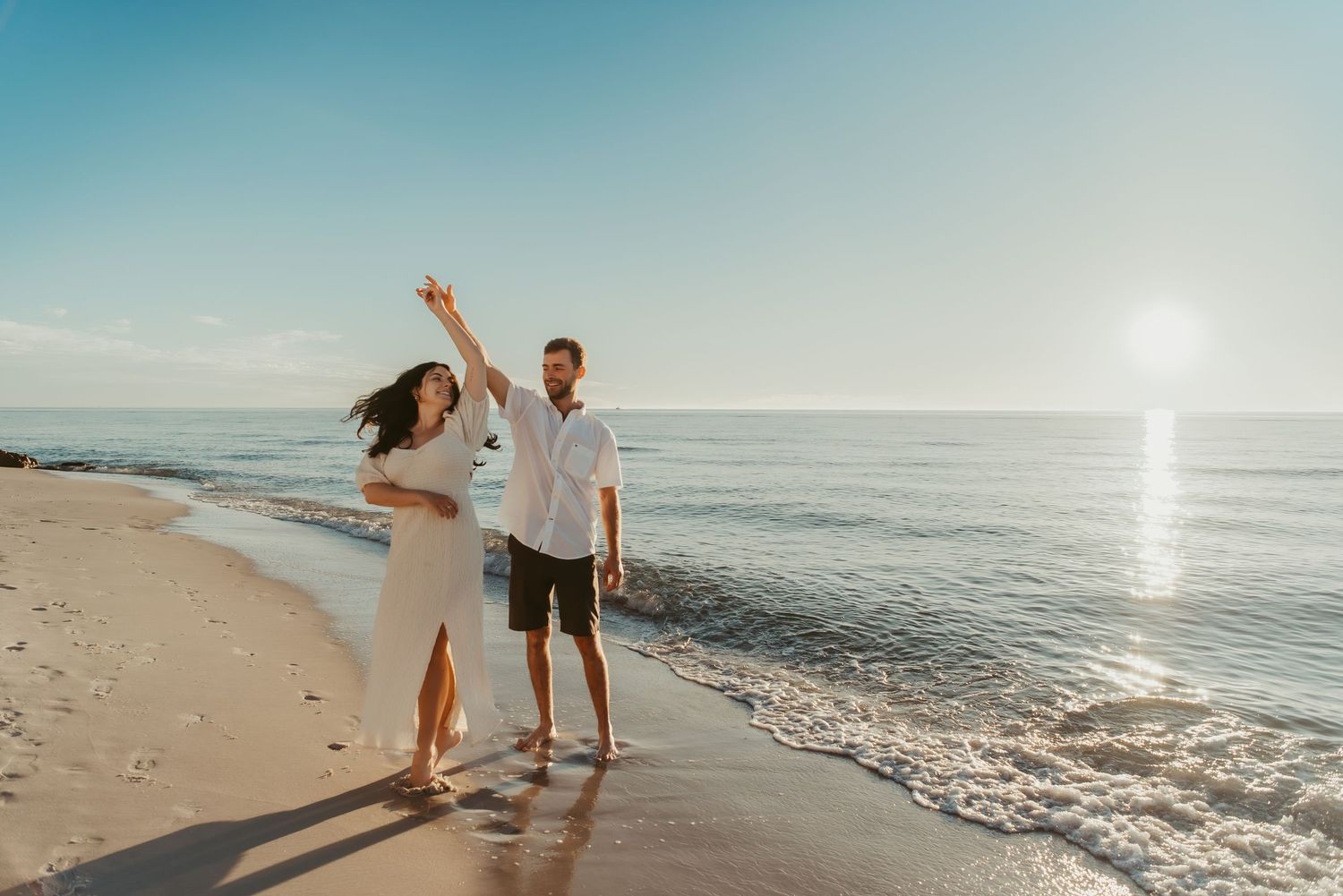 Couple dancing joyfully on beach at sunset with ocean waves.