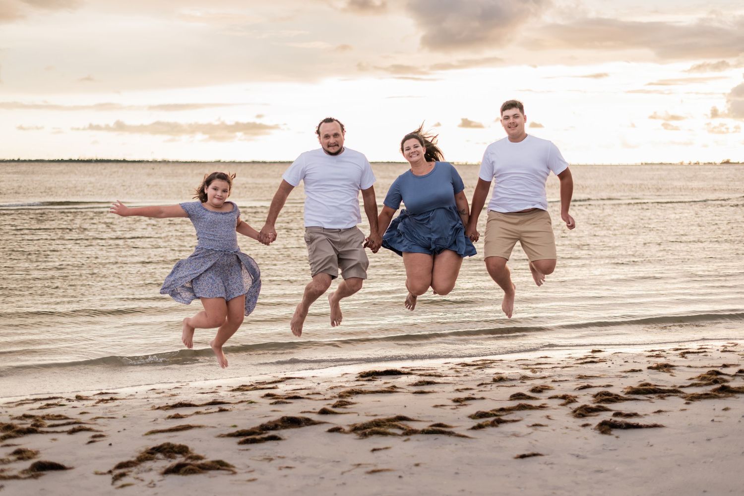 Group of people perform synchronized jump at sunset on sandy beach with ocean waves in background.