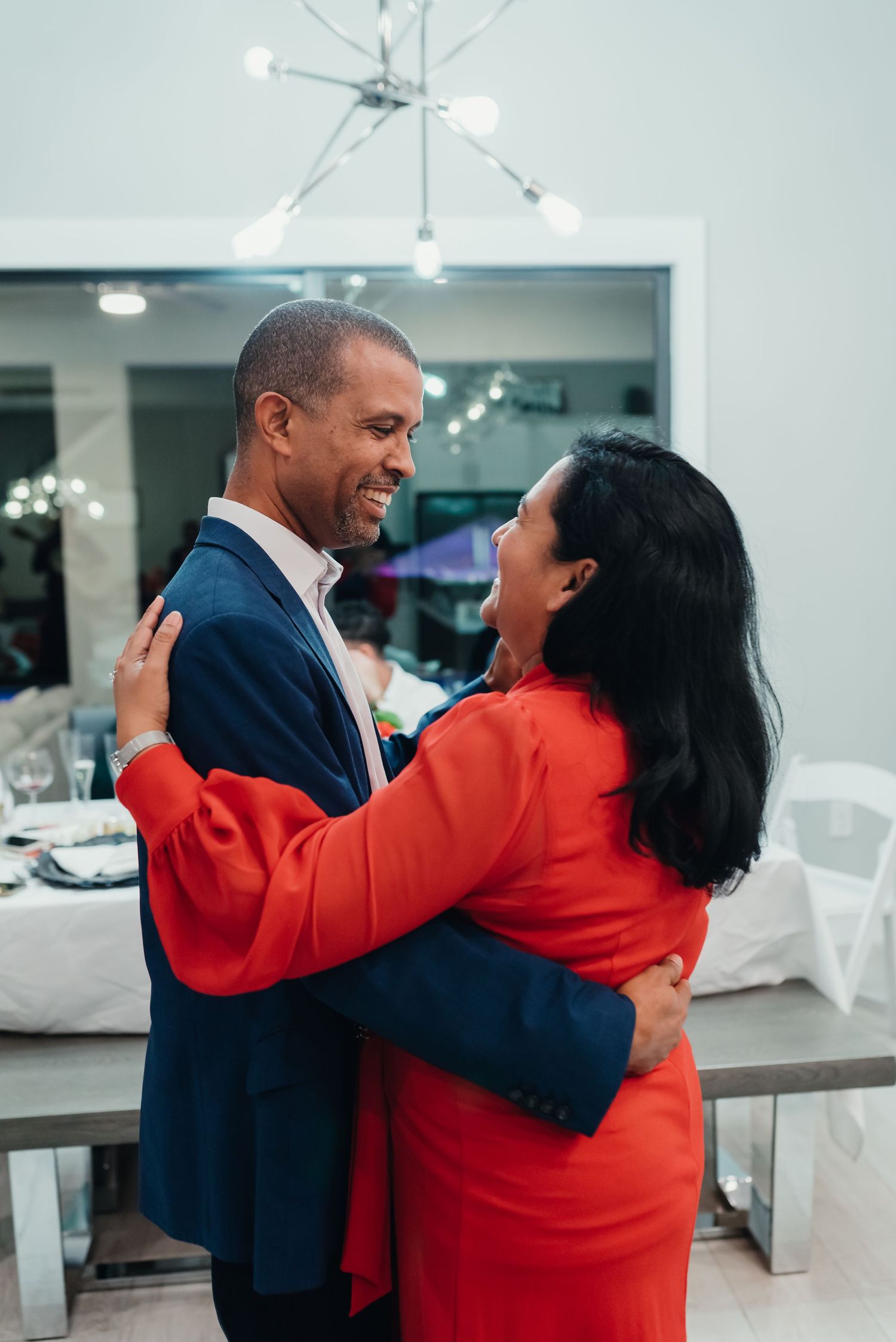 A couple in formal attire share an intimate dance moment, with a person in navy suit and another in red dress embracing.