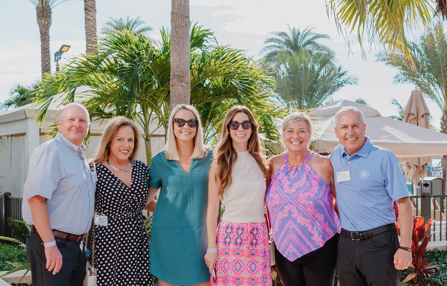 Group of people at a resort with palm trees posing together outdoors on a sunny day.