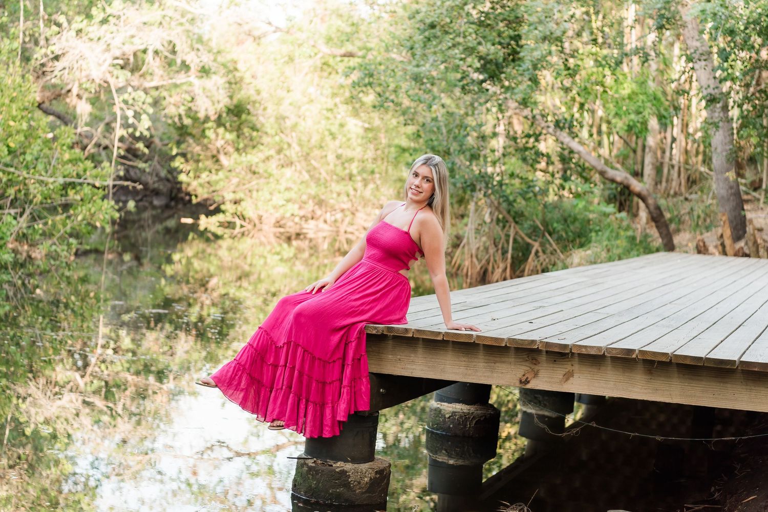 Someone in a bright pink dress poses and dances across multiple images in an outdoor nature setting near a footbridge.