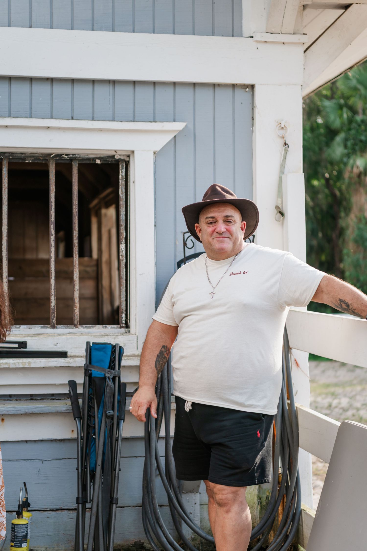 A person in a white shirt and cowboy hat stands near a blue and white building with windows.
