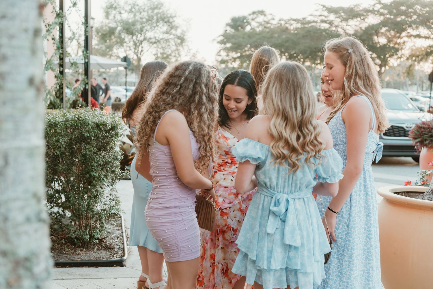 A group in pastel dresses and spring outfits gather together for casual conversation at an outdoor venue.