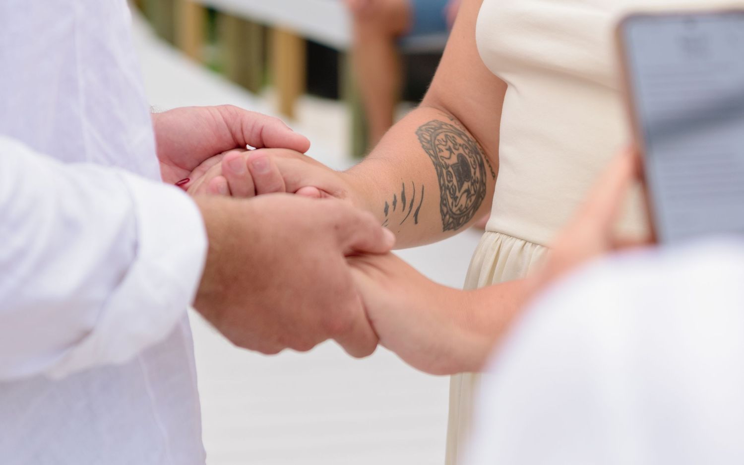 Close-up view of hands exchanging wedding vows with visible tattoo detail during outdoor ceremony.