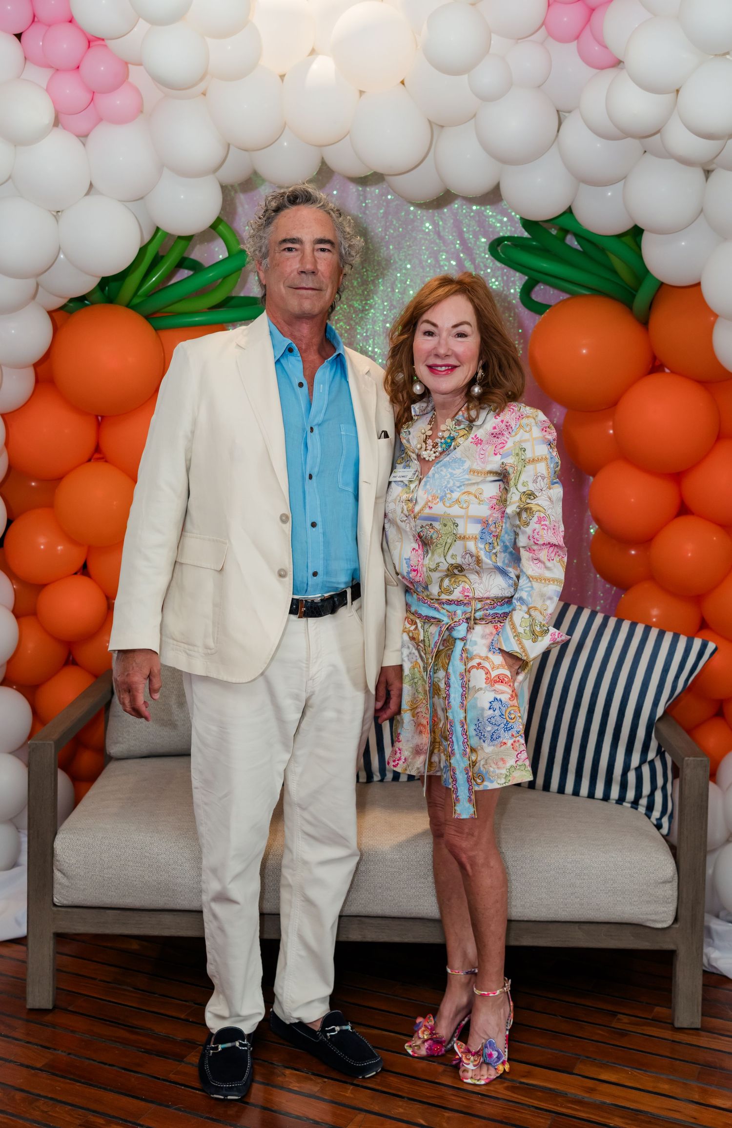 Elegantly dressed couple posing in front of colorful balloon wall with carrot decorations at a festive event.