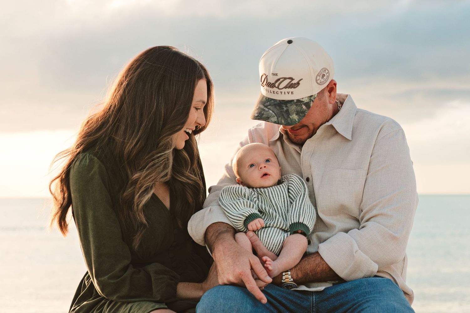 A couple shares tender moments with their baby at the beach during sunset while wearing casual attire.