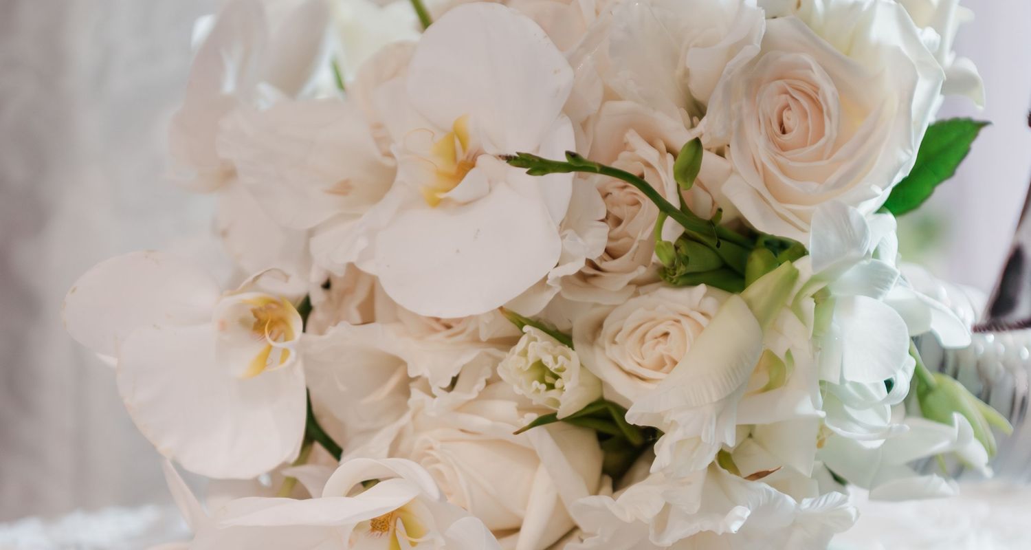 Elegant all-white wedding bouquet featuring orchids and roses in a soft romantic arrangement.